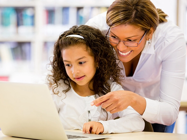 Una educadora y una estudiante pequeña usando una computadora